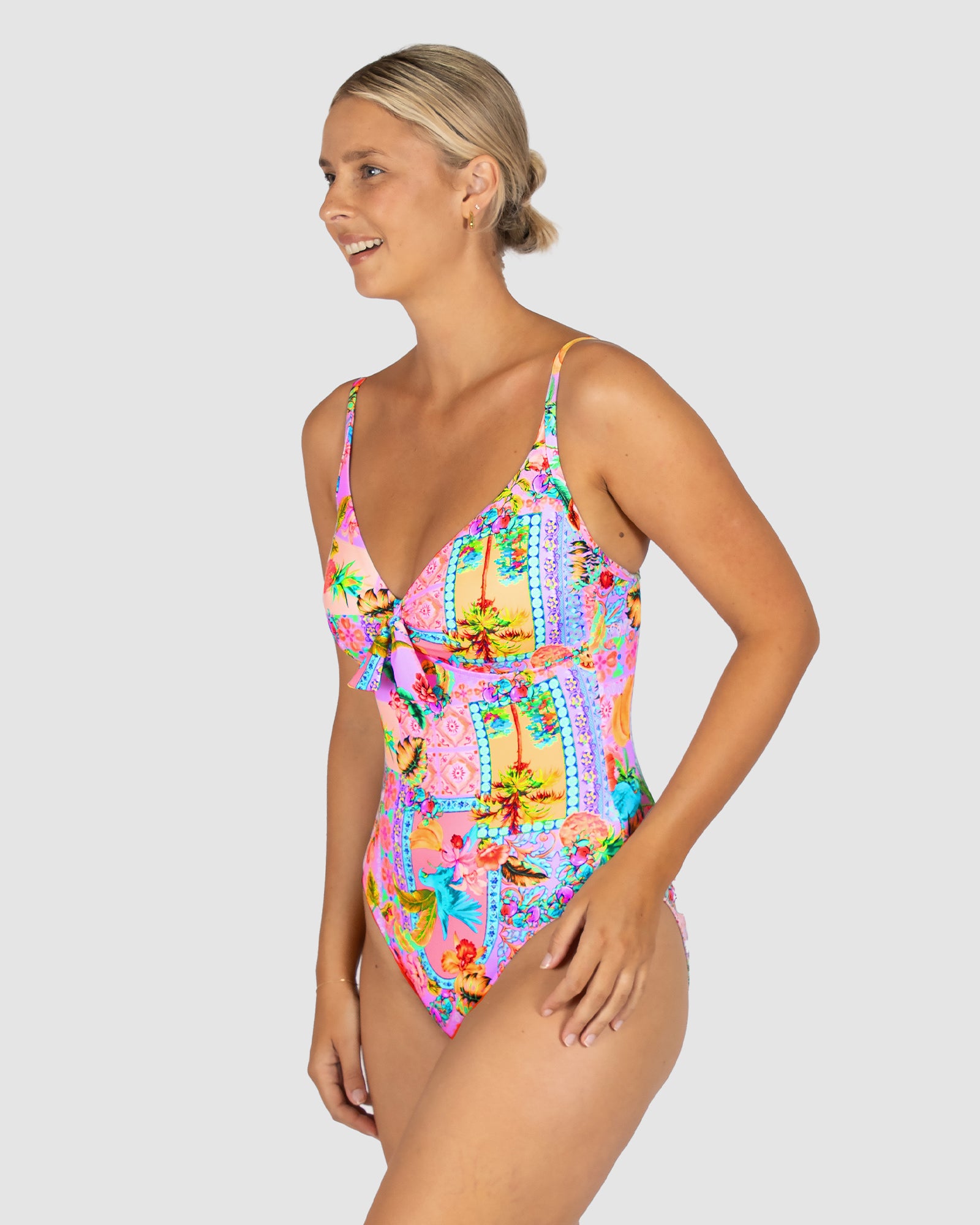 Woman wearing a colorful floral one-piece swimsuit on a light gray background