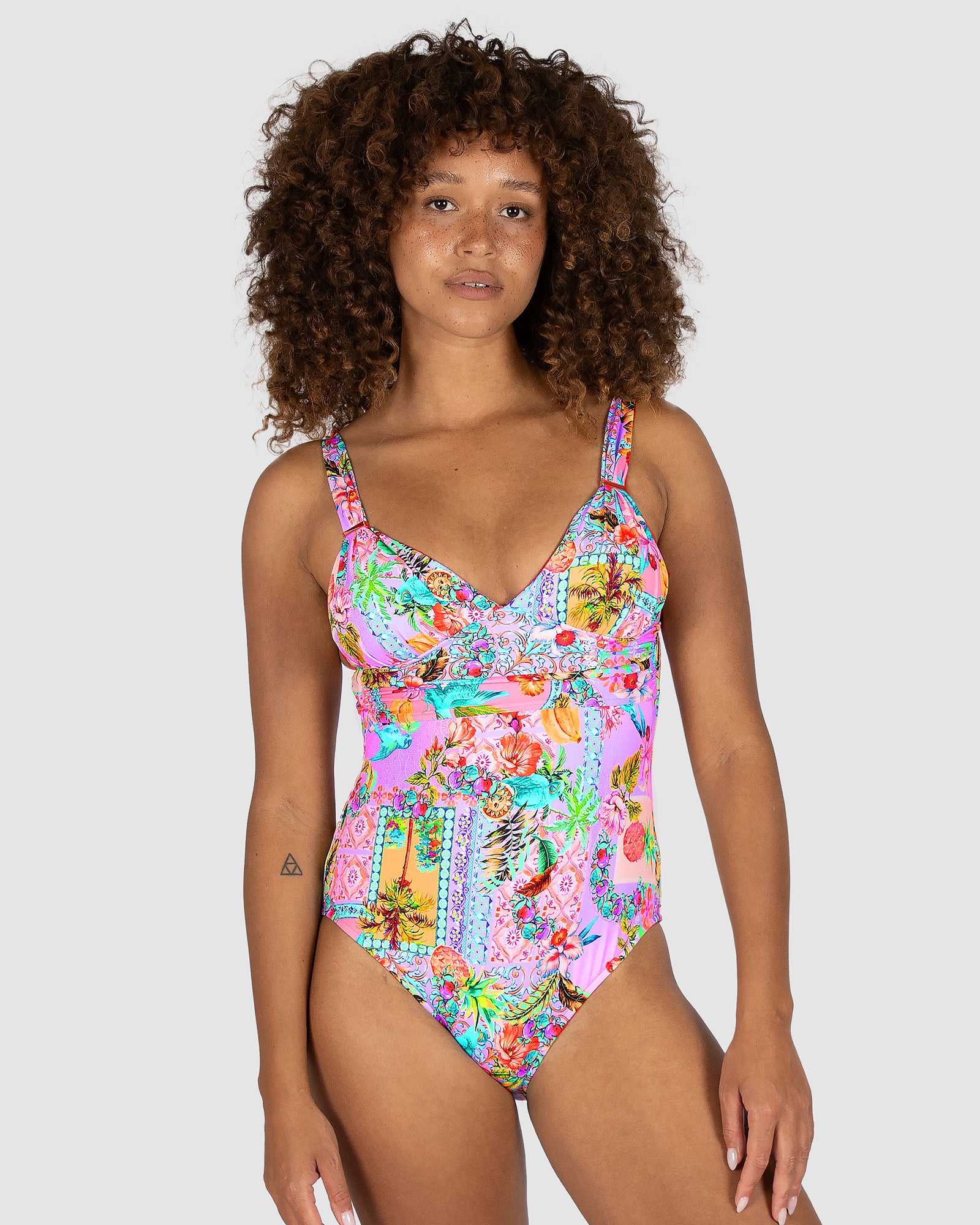 Baku Sardinia Grecian One Piece Swimsuit in bold tropical print, featuring soft removable cups, ruched detailing, rose gold bar trim, and adjustable convertible straps for a flattering fit.